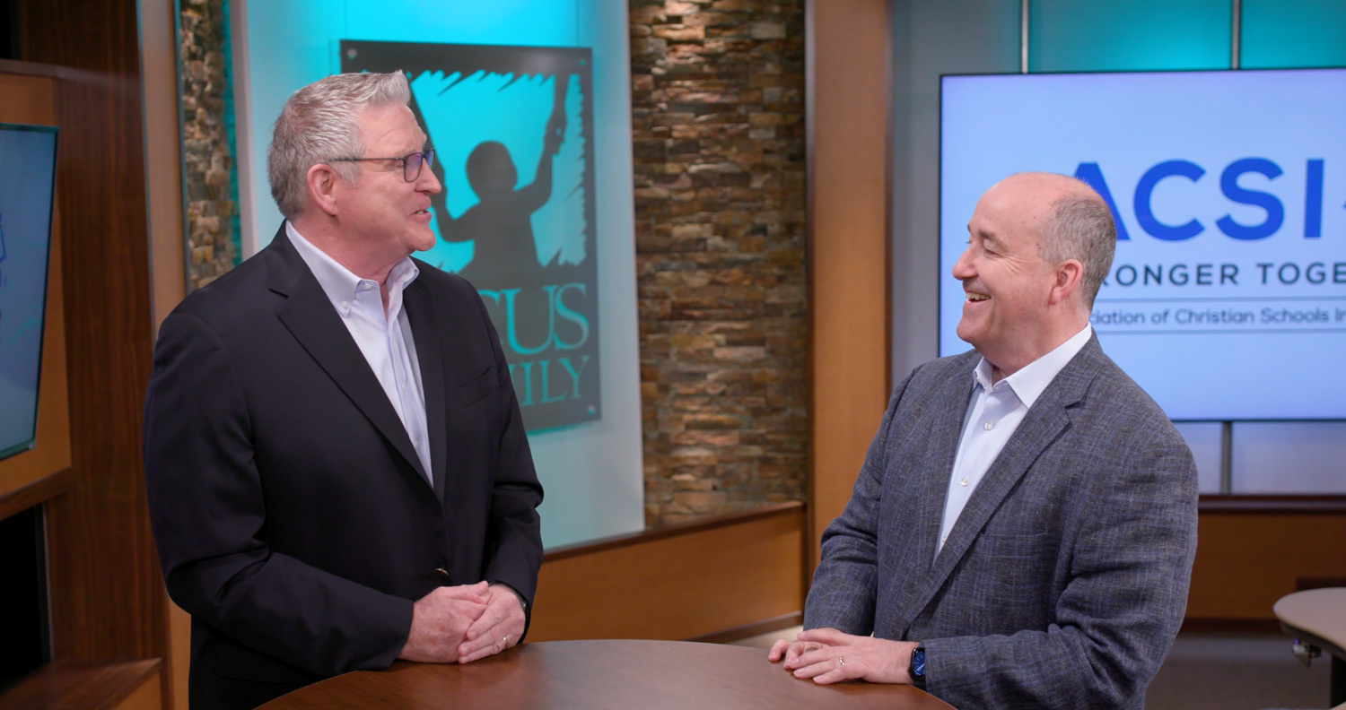 Two men talk around a table.