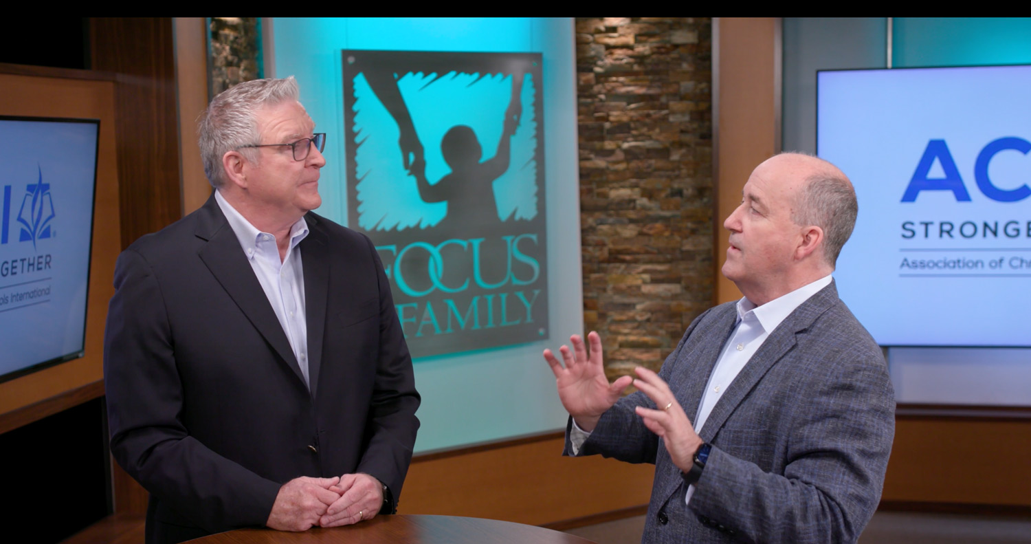 Two men talk around a table.